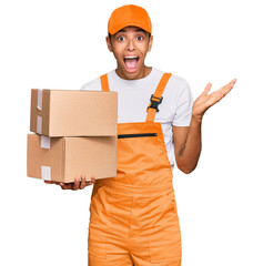 Wall Mural - Young handsome african american man holding delivery package celebrating victory with happy smile and winner expression with raised hands