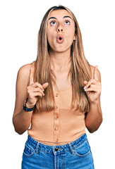 Poster - Hispanic young woman wearing casual summer shirt amazed and surprised looking up and pointing with fingers and raised arms.