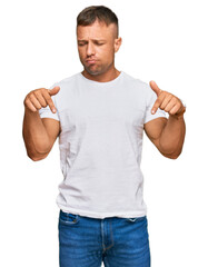 Canvas Print - Handsome muscle man wearing casual white tshirt pointing down looking sad and upset, indicating direction with fingers, unhappy and depressed.