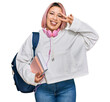 © Krakenimages.com - Hispanic woman with pink hair wearing student backpack and headphones doing peace symbol with fingers over face, smiling cheerful showing victory