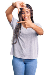 Wall Mural - Young african american woman with braids wearing casual clothes smiling making frame with hands and fingers with happy face. creativity and photography concept.