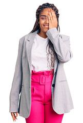 Canvas Print - Young african american woman with braids wearing business clothes covering one eye with hand, confident smile on face and surprise emotion.