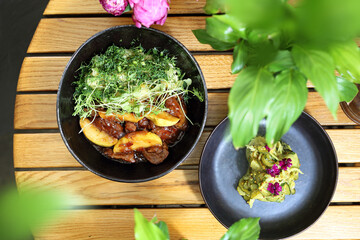 Stewed chicken liver with apple, served with pickled cucumber salad, on a wooden background, top view, selective focus.