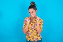 Beautiful Brunette Woman Wearing Colourful Shirt Over Blue Background Clenches Fists And Awaits For Something Nice Happened Looks Away Bites Lips And Waits Announcement Of Results
