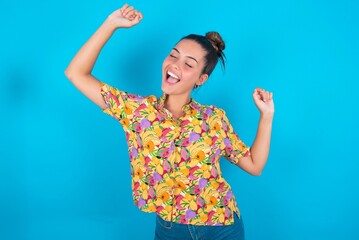 Photo of upbeat beautiful brunette woman wearing colourful shirt over blue background has fun and dances carefree wear being in perfect mood makes movements. Spends free time on disco party