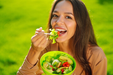 Young woman  enjoying a healthy meal. Woman eating salad outdoor on sunny day.  Concept picnic. Vegetarian.