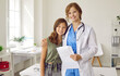 © Studio Romantic - Portrait of doctor and teen child at clinic. Happy beautiful pediatrician with clipboard together with pretty school girl standing in medical office, looking at camera and smiling. Health concept