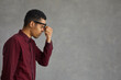 © Studio Romantic - Profile view of a tired dark-skinned young man rubbing his eyes after doing hard work. Concept of eye fatigue from the computer and fatigue from work. Gray background. Place for text. Banner.