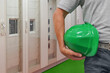 © polack - Close-up of worker holding green hard hat on against the on electrical terminal cabinets background. Hand of worker with green hard hat on electrical cabinets background. Electrician Industry workers
