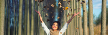 Young Smiling Woman Throwing Leaves In The Air In Autumn Forest