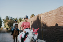 2 Young Female Riders Ride Their Horses Through An Alleyway