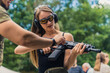 © PoppyPix - Helpful instructor explains how to use a rifle to his female caucasian long-hared client who is wearing protective shooting range gear. Outdoor medium shot. High quality photo