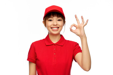 Poster - profession, job and people concept - happy smiling delivery woman in red uniform showing ok gesture over white background