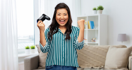 people, leisure and gaming concept - happy woman playing video game with gamepad celebrating success over home background