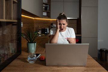 Young woman surprised negative facial reactions on positive result on pregnancy test. Young girl talking on video call on laptop computer with her mother complaining that she is pregnant. Unwanted