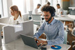 © Kostiantyn - Businessman in headphones working laptop while sitting in modern office on colleagues background