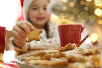 Wall Mural - Little girl taking tasty Christmas cookie from plate at table, closeup