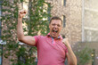 © sommersby - Excited millennial man keeping fists up and screaming with happiness, standing outdoors. Middle age man very happy  doing winner gesture with arms raised and screaming for success outdoor at city