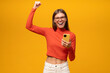 Lucky excited woman holding smartphone making winner gesture shouting yes on yellow background