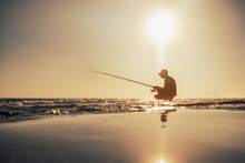 Fishermen Silhouette Fishing On The Seashore In The Evening Under Warm Sun