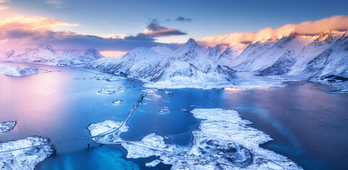 Wall Mural - aerial view of sea, snowy islands, mountains, road, sky with pink clouds at sunset in winter. lofote