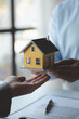 A housing salesman holds a model of a house and sends it to customers as an example, a sample house project where a salesperson advises customers. The concept of selling houses in the project.