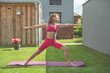 Blonde teen girl doing yoga exercises on green grass