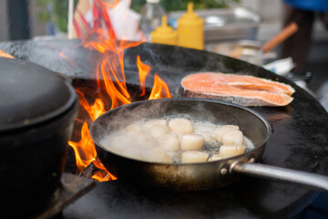 Process of cooking scallop meat, salmon on black brazier at summer outdoor food market: close up. Seafood, barbecue, gastronomy, cookery, street food concept