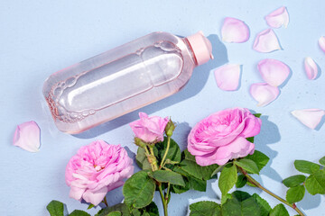 Bottle with clear micellar water on a blue background top view and Pink Damask rose buds. . Lotion for cleansing the skin. Liquid beauty product in plastic packaging.Natural beauty product concept.