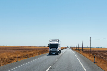 Canvas Print - Refrigerator truck driving on a straight road, with a flat horizon and a clear sky.