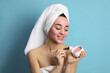 Woman applying pomegranate face mask on light blue background