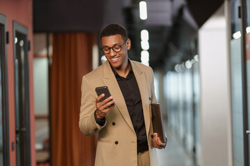 Handsome smiling african businessman using phone while standing in modern coworking