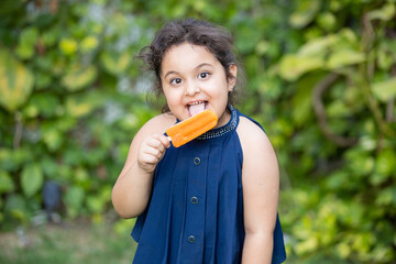 Happy cute little indian girl child enjoying ice lolly or ice cream at park.