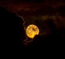 Red Full Moon Rising Or Emerging From Clouds In Silhouette Illuminated By Moonlight.