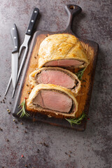 Sliced Beef Wellington on a wooden board with a sprig of rosemary on a grey background. Vertical top view from above