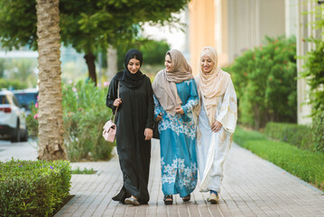 Wall Mural - Arabic women wearing traditional abaya dress meeting and having fun in Dubai - Happy beautiful muslim females bonding outdoors in the city