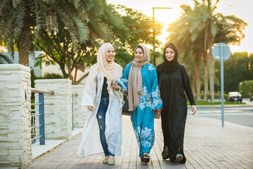 Wall Mural - Arabic women wearing traditional abaya dress meeting and having fun in Dubai - Happy beautiful muslim females bonding outdoors in the city