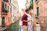 Fototapeta Uliczki - Happy beautiful couple of lovers doing romantic trip in Venice, Italy - Tourists visiting historic town of Venice and kissing in a traditional narrow street canal