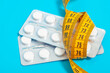 © Lyubov - Tablets in transparent plates wrapped with a centimeter tape on a blue background close-up. The concept of weight loss, fat burning, vitamins, sports nutrition.