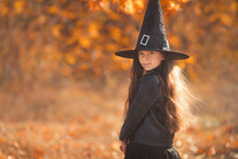 Portrait Of Brunette Little Teen Girl In Witch Costume And Hat For Halloween In Forest 