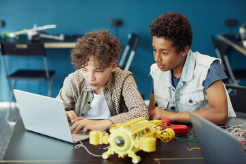Wall Mural - Portrait of two teenage boys using laptop and programming robot during engineering class in school