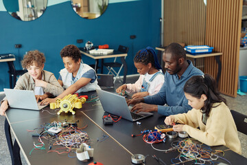 Wall Mural - High angle view at diverse group of children with male teacher building robots during engineering class in school
