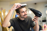 Young man hairdresser drying and combing his own hair in his hair salon