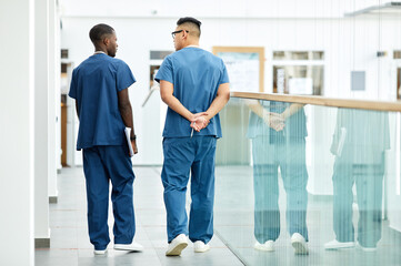 back view full length of two doctors wearing blue uniform walking in hall of modern clinic, copy spa