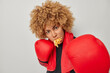 Fitness woman has mouth full of french fries stands in defensive pose exercises punches wears red boxing gloves clenches fists focused angrily at camera stands indoors. Boxing and sport concept