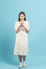 Wall Mural - Beautiful young asian woman in white dress with flower pattern using smartphone isolated on blue background