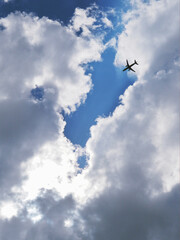 Wall Mural - The passenger airplane is flying far away in the blue sky and clouds. Dramatic clouds with the sun shining through them. Aircraft in the air. Vertical illustration. Passenger air transportation