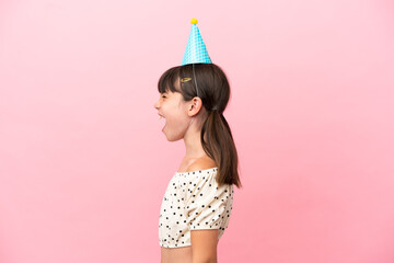 Little caucasian kid with birthday hat isolated on pink background laughing in lateral position