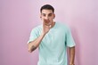 © Krakenimages.com - Handsome hispanic man standing over pink background hand on mouth telling secret rumor, whispering malicious talk conversation