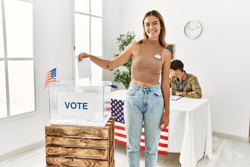 Canvas Print - Young blonde girl voting putting envelop in ballot box looking positive and happy standing and smiling with a confident smile showing teeth